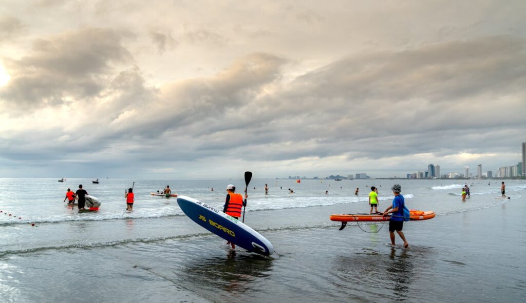 Group of people paddleboarding and enjoying water sports on a cloudy beach day.
